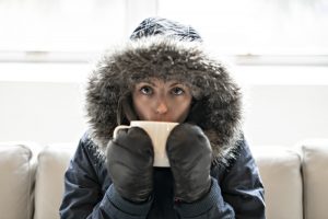 person-indoors-with-coat-and-mittens-on-drinking-hot-tea